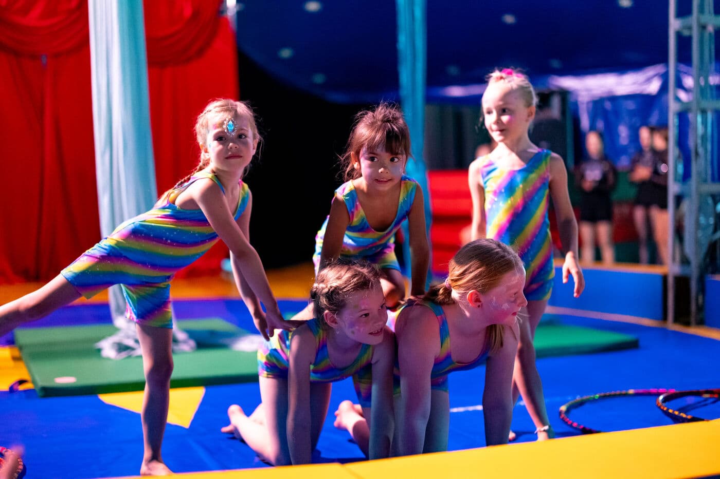Kinder in Regenbogen-Kostümen bauen eine Pyramide in der Manege
