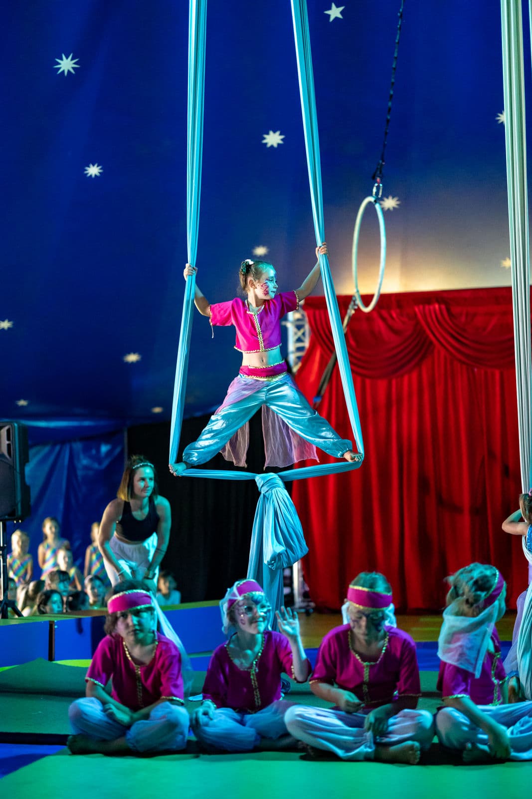 Mädchen im Kostüm am Vertikaltuch über der sitzenden Gruppe in der Manege